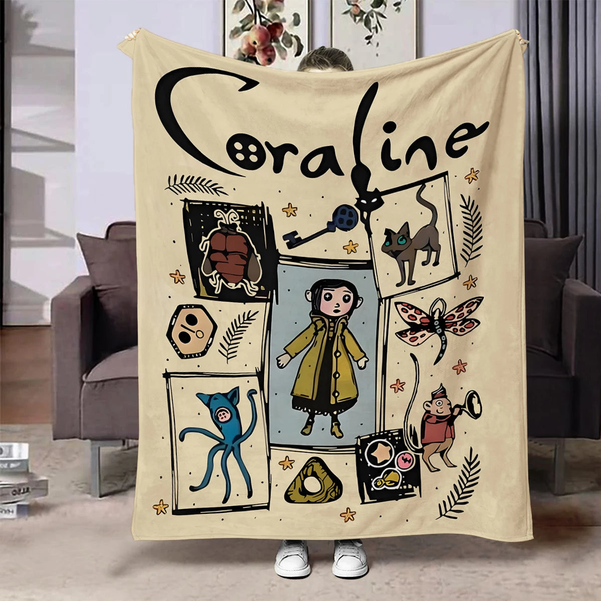 A cream colored flannel throw blanket featuring a black line drawing of the name Coraline and various whimsical illustrations