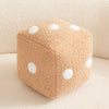 A beige plush dice cube cushion with white polka dots resting on a light surface.