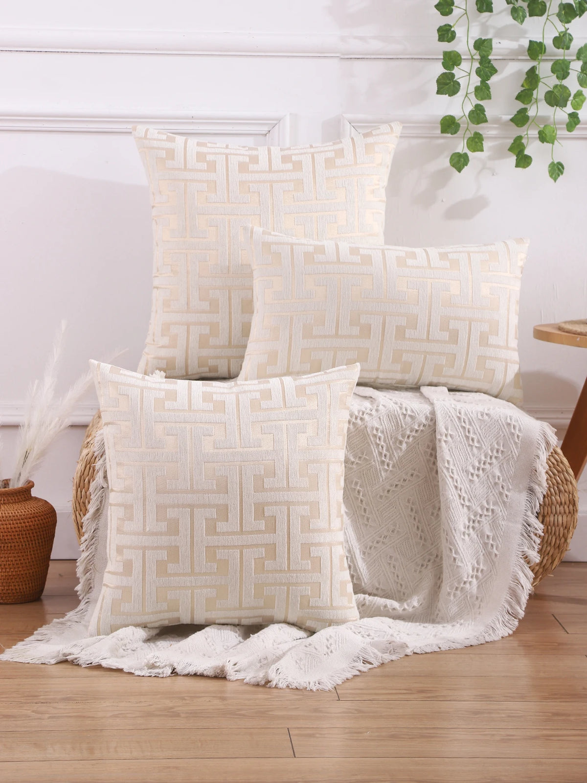 A collection of cream and beige embroidered throw pillows featuring a geometric Greek key pattern on a wooden surface.