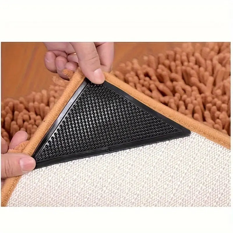A hand is pressing a black, triangular non-slip carpet gripper onto a beige carpet surface.