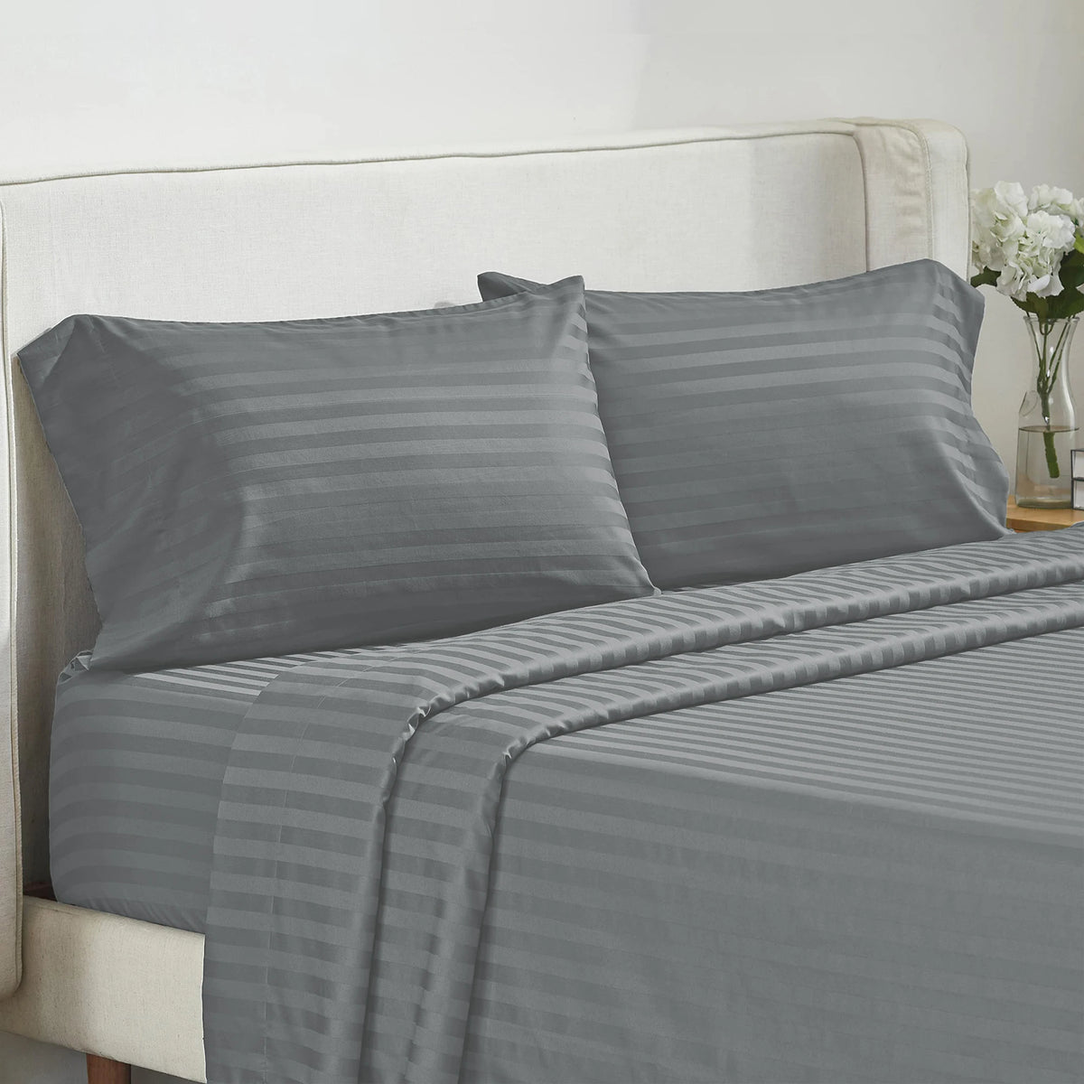 A set of gray striped bedding, including pillows and a fitted sheet, displayed on a bed.