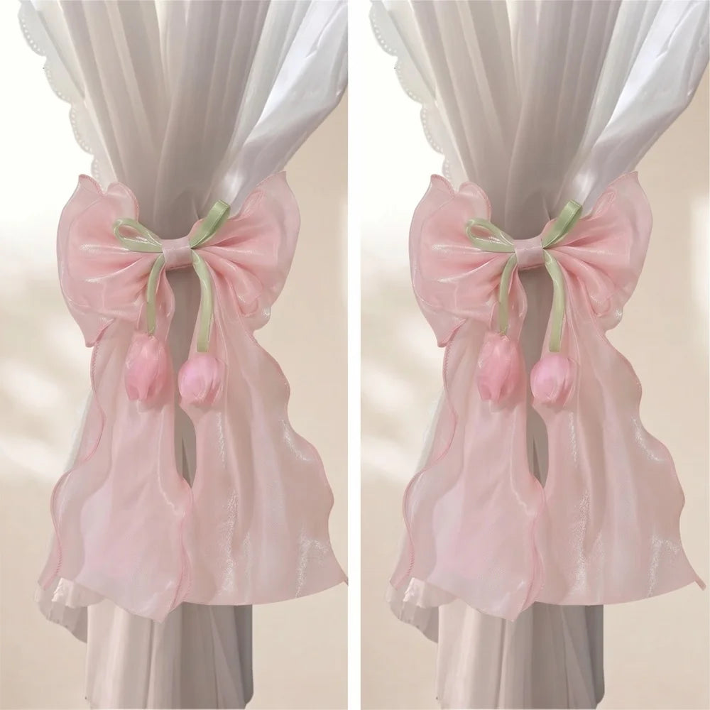 A pair of pink sheer ribbon bow curtain tiebacks displayed on a hanger.