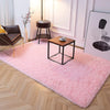 A pink plush area rug with a fluffy texture is displayed on a light wood floor in a bright room.