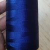A spool of dark blue high tenacity polyester sewing thread with a yellow plastic core is held in a hand.
