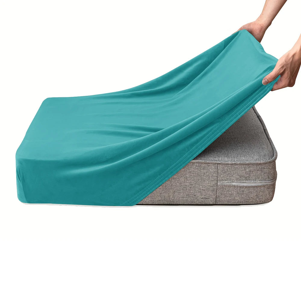 A teal velvet stretchy sofa seat cover is being placed onto a gray cushion.