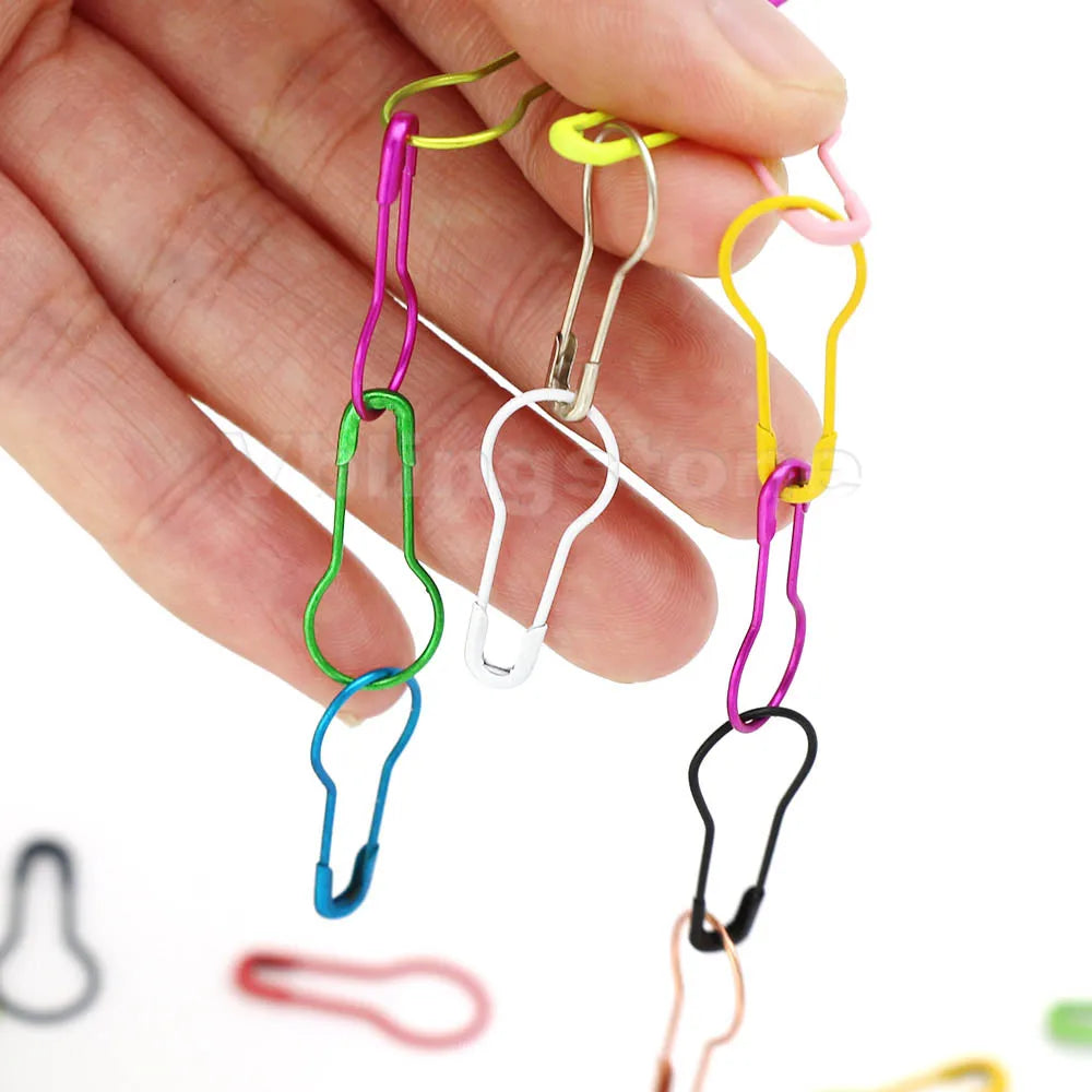 A hand holds several colorful gourd-shaped locking safety pins for knitting and sewing.