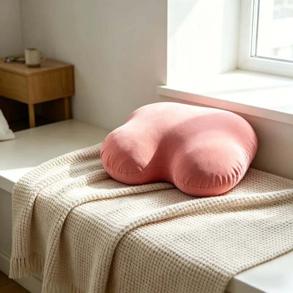 A pink memory foam contour chest pillow resting on a cream knitted blanket near a window.