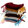 A stack of velvet drawstring jewelry gift bags in various shades including maroon, gold, gray, brown, and blue.