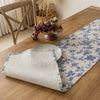 A checkered table runner with a blue floral pattern laid on a wooden table next to a bowl of grapes.