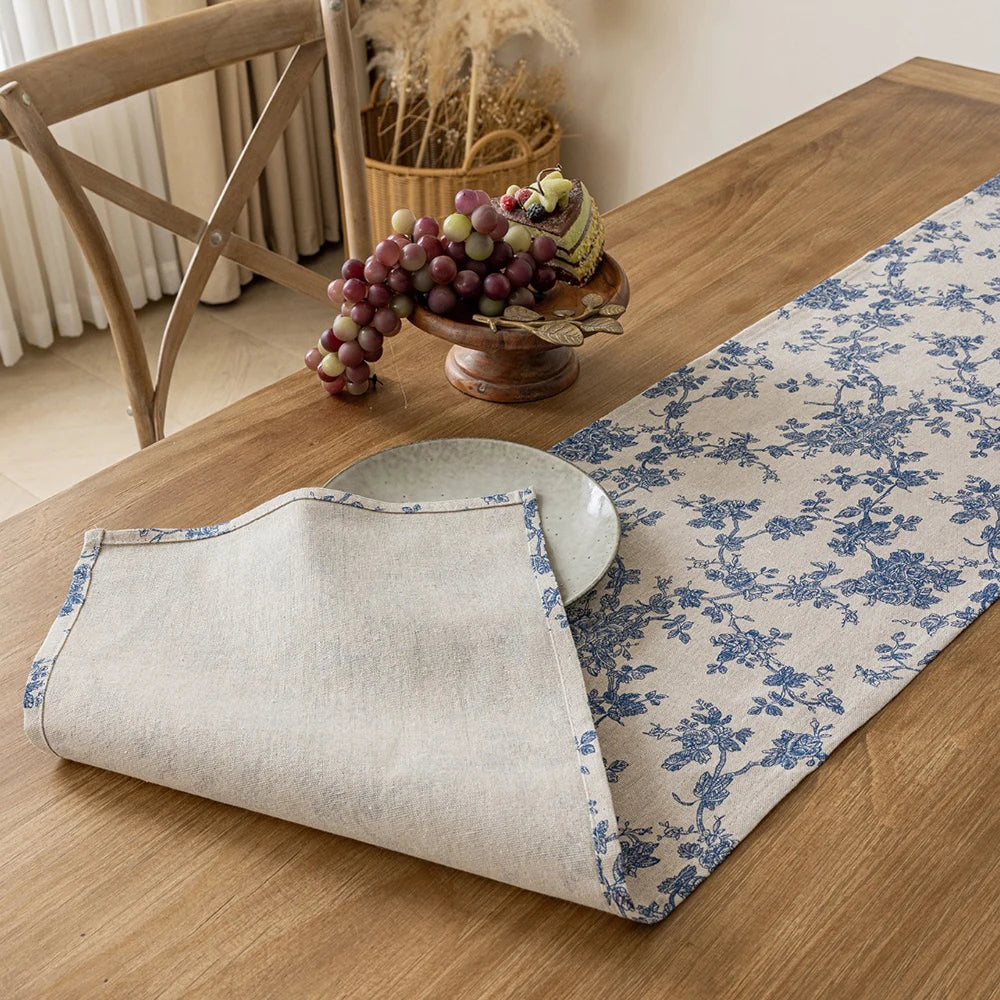 A checkered table runner with a blue floral pattern laid on a wooden table next to a bowl of grapes.