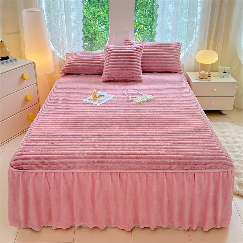 A pink plush bed skirt linen set with matching pillows and bedding displayed on a light wood bed frame.