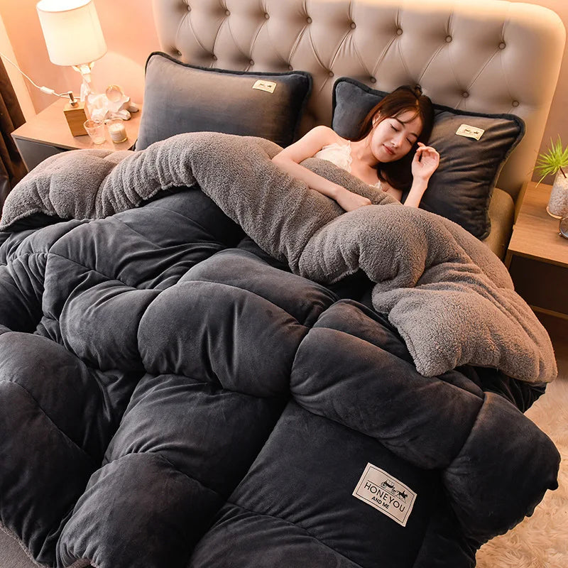 A person relaxing under a large dark gray plush fleece blanket on a bed with a tufted headboard.
