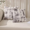 A pair of fluffy gray and white faux rabbit fur decorative throw pillows resting on a light-colored surface.