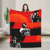 A red and black blanket featuring illustrations of Western figures, including a gunslinger and a cowboy.