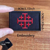 A black embroidered patch featuring a red cross design on a wooden surface.