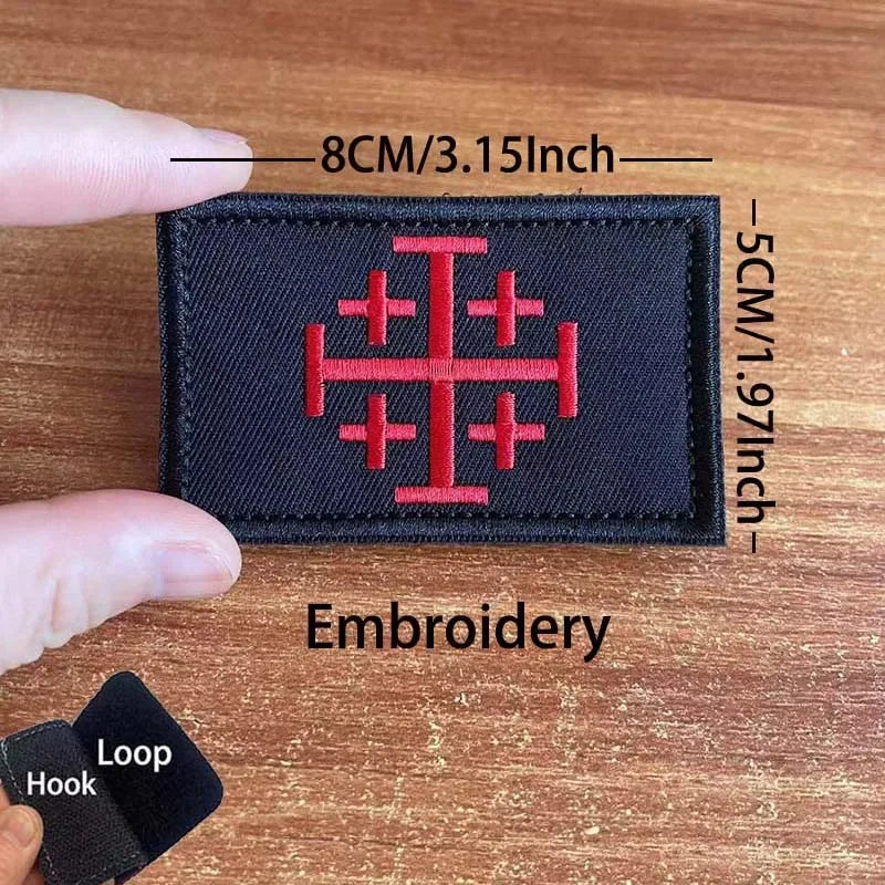 A black embroidered patch featuring a red cross design on a wooden surface.