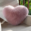 A fluffy pink heart-shaped fox fur throw pillow resting on a light-colored outdoor chair.