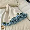 A hand knitted floral rose bouquet throw blanket in cream and blue colors resting on a light-colored surface.