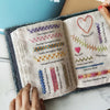 An open embroidery stitch book showing various hand embroidery stitches on a beige fabric.