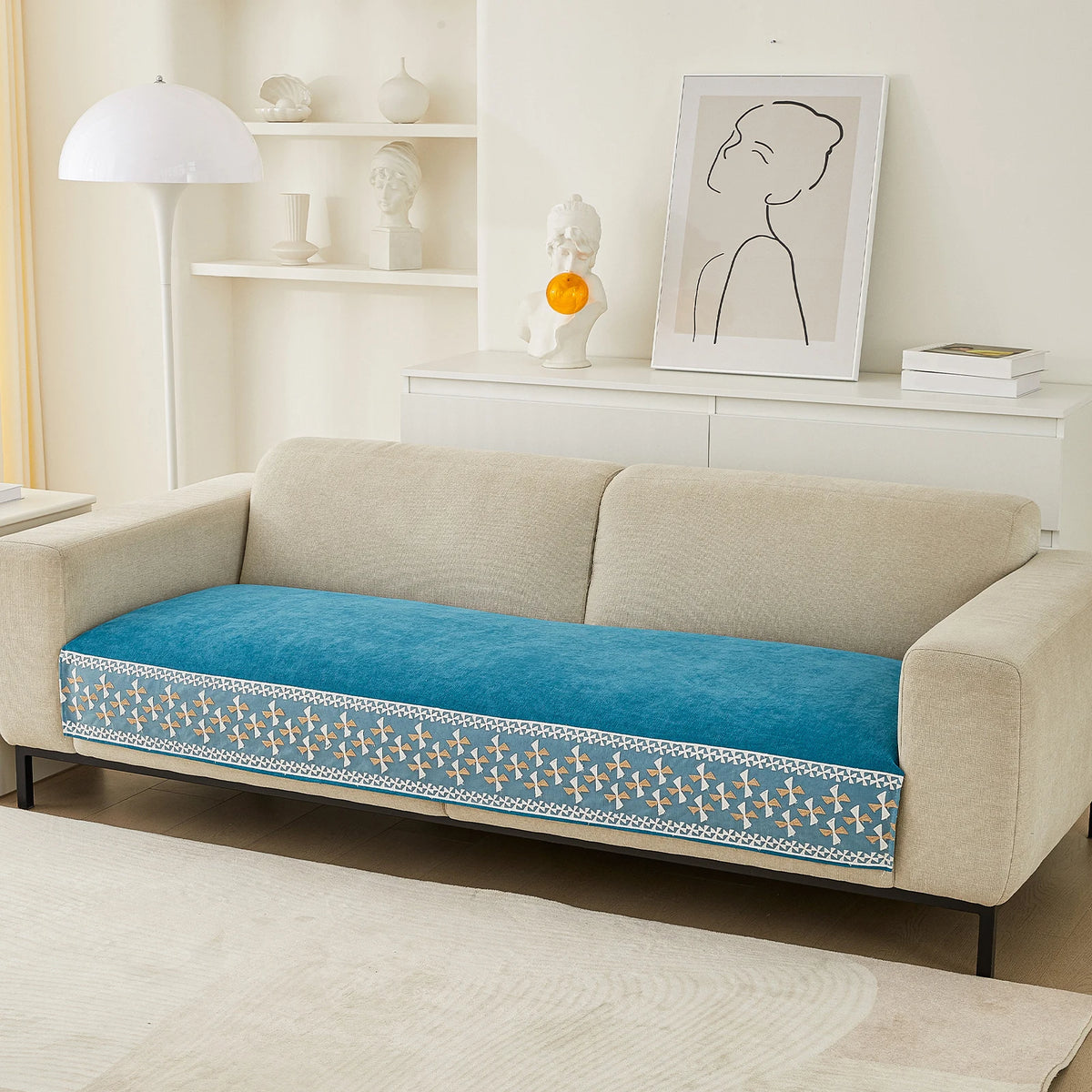 A beige sofa with a blue quilted cover featuring a white lace trim and displayed decor.