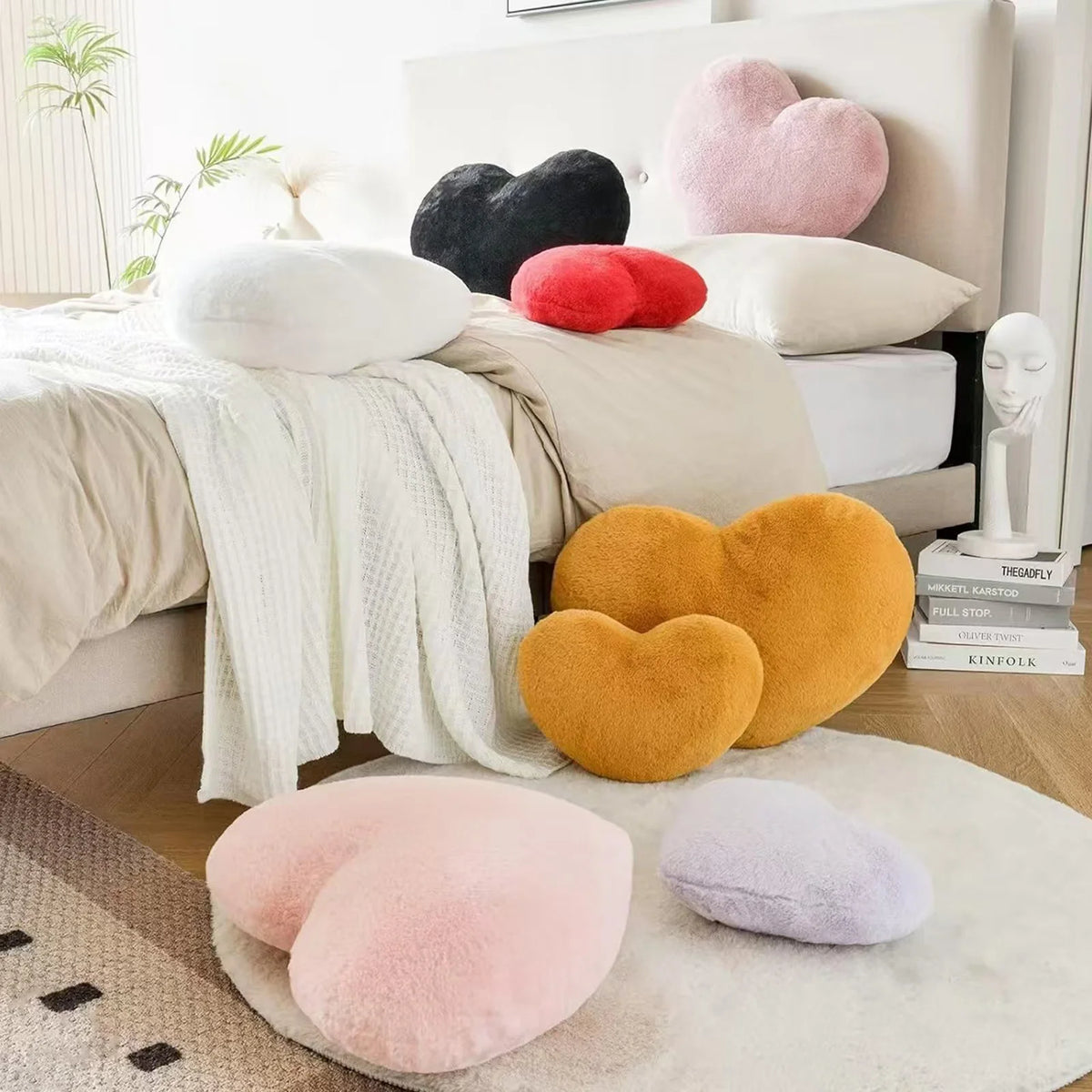 A collection of heart-shaped throw pillows in pink, yellow, and black resting on a beige bed.
