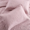 A close-up of a pink embroidered cotton quilted pillow cover set with swirling floral patterns.