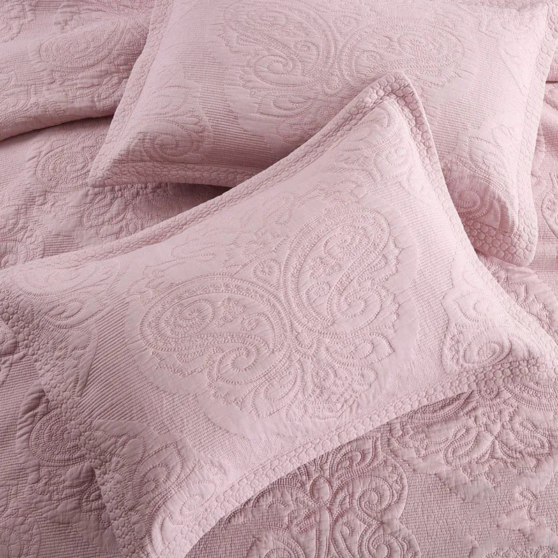 A close-up of a pink embroidered cotton quilted pillow cover set with swirling floral patterns.