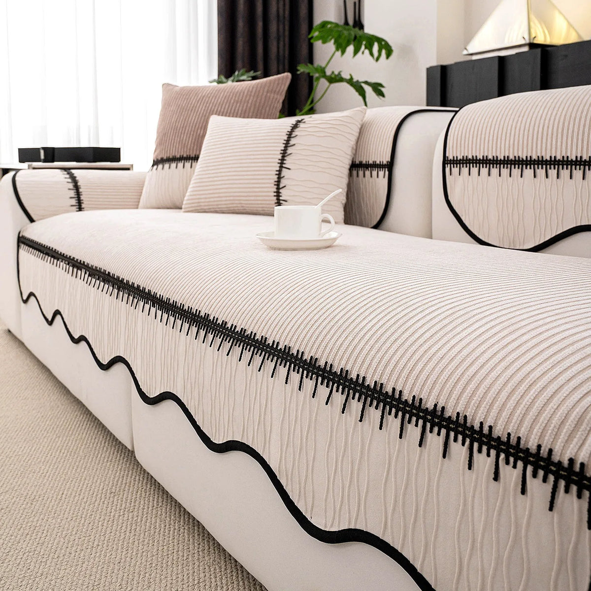 A beige pleated sofa cover with black trim and textured fabric displayed on a white sofa.
