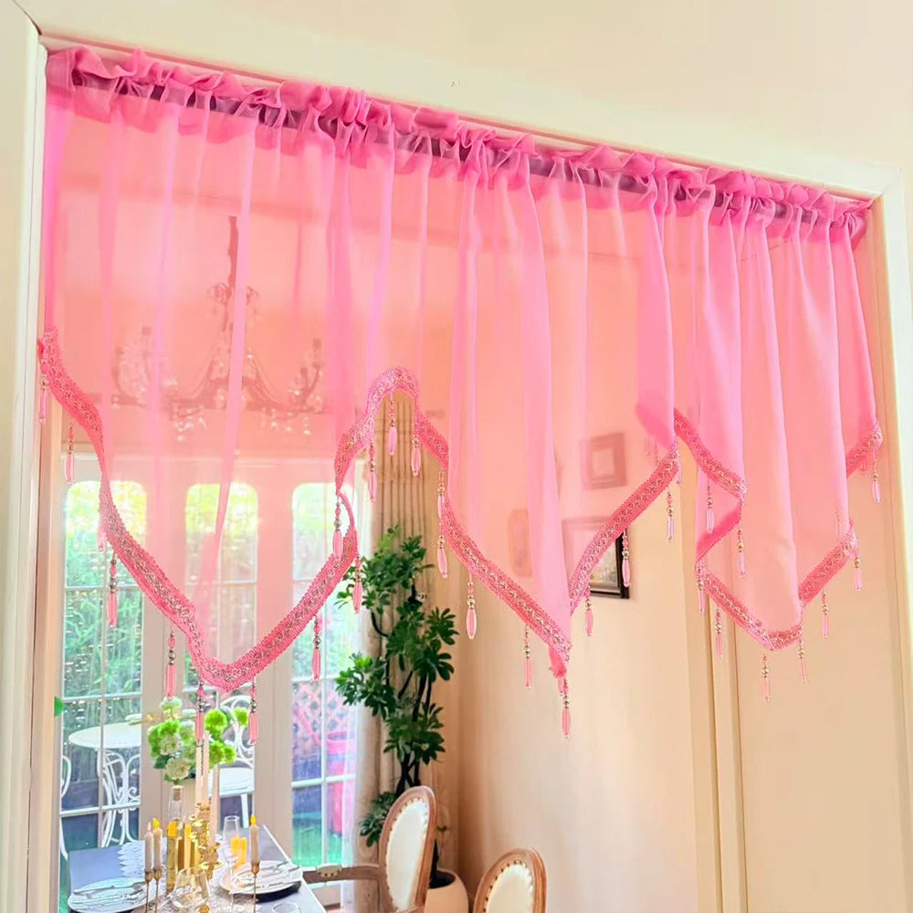 Pink sheer curtain with heart lace and tassels hanging in a window frame.