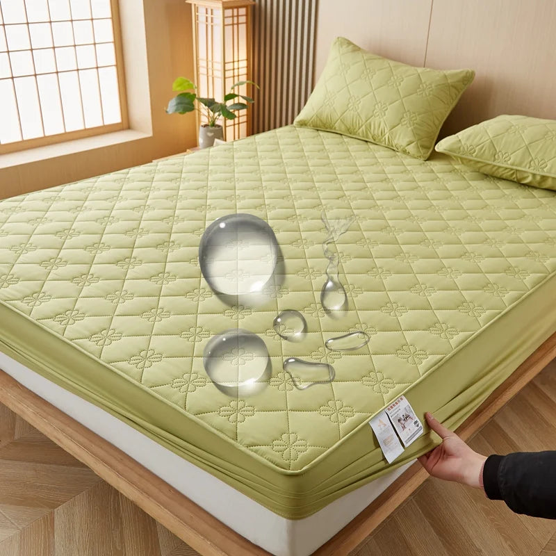 A light green waterproof mattress protector is shown on a bed, featuring decorative quilted patterns and clear glass-like obj