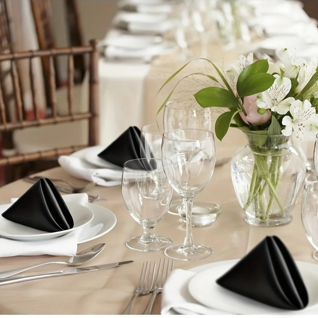 A close-up of black silky satin dinner napkins and silverware set on a table for an event.