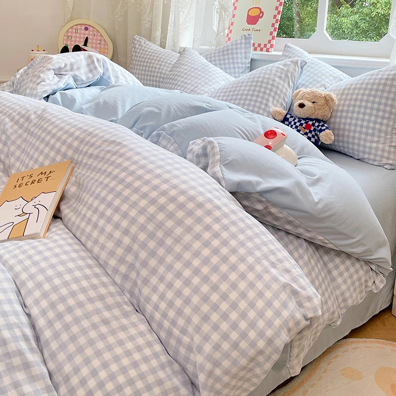 A light blue and white checkered duvet cover set with pillows and a teddy bear on a bed.