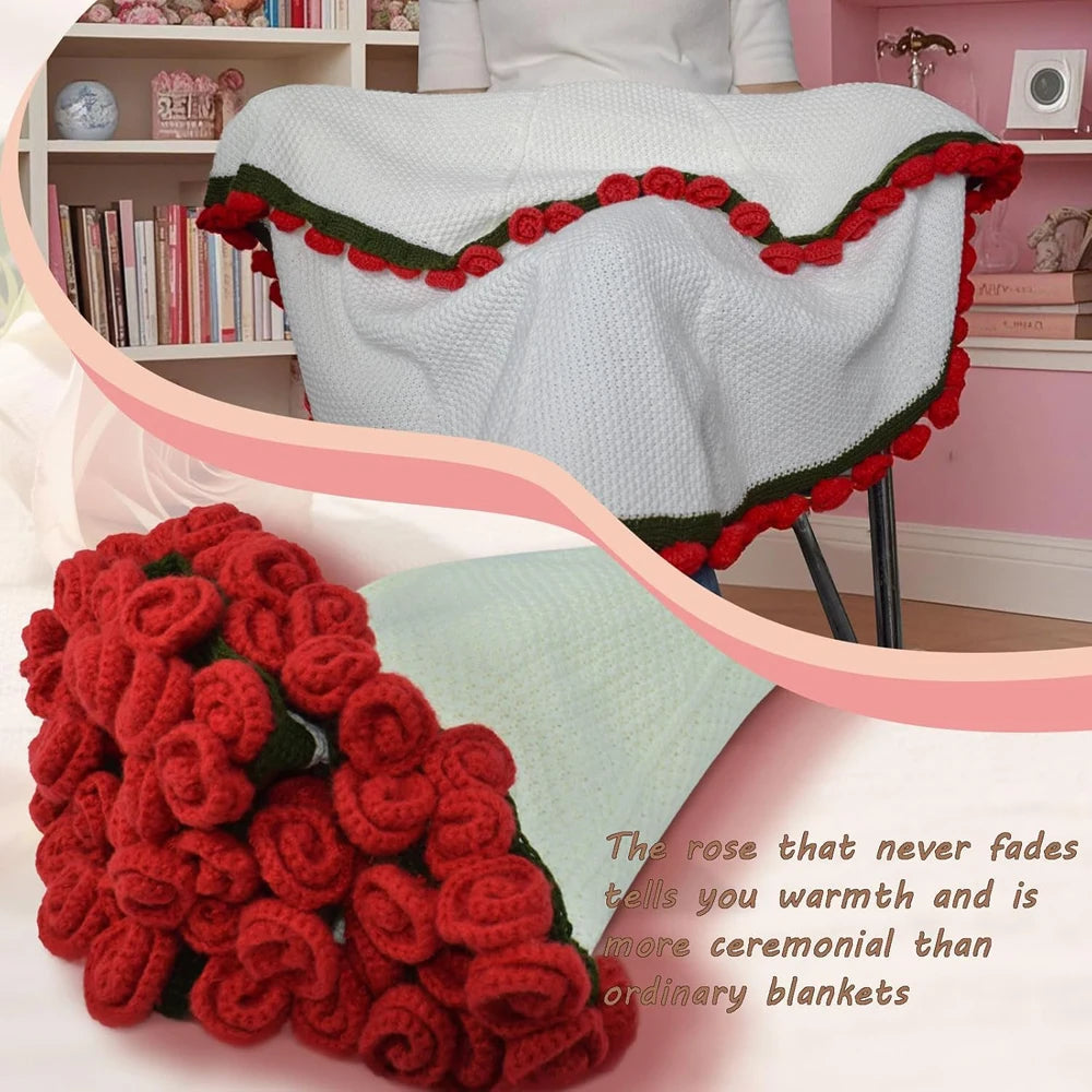 A knitted throw blanket with a floral bouquet design in red and green yarn is displayed on a light pink background.