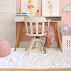A pink and white room decor featuring a wooden desk, a white chair, and colorful art prints on the wall.