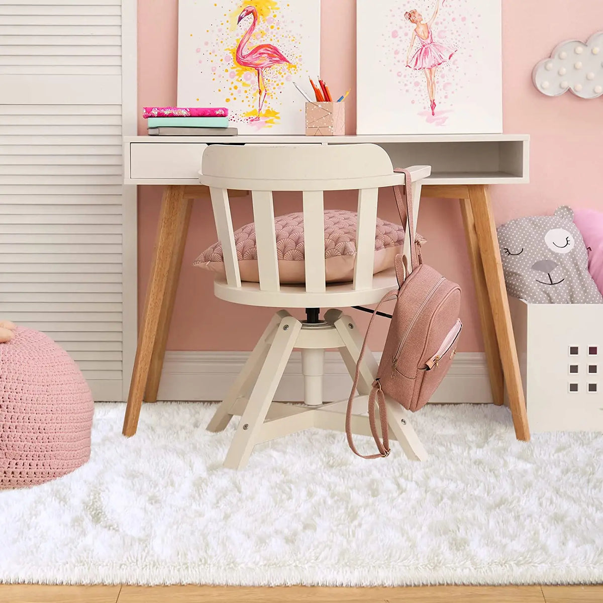 A pink and white room decor featuring a wooden desk, a white chair, and colorful art prints on the wall.