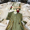 A long, sage green cheesecloth table runner is laid down on a white tablecloth for a rustic boho dining setting.
