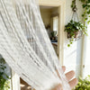 A hand holds sheer white lace tassel door curtains draped in a vertical fold.