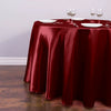 A deep red satin round table cloth set for elegant decor with white plates and silverware.