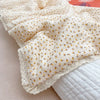 A close-up of a floral print muslin blanket for baby in cream and yellow, folded on a light pink surface.