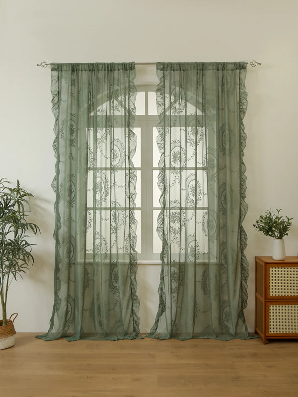 Light green sheer lace curtains hanging over a window with a white frame and wooden floor.