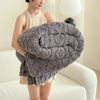 A woman is holding a thick, gray ultra-soft coral fleece blanket rolled up on a white sofa.