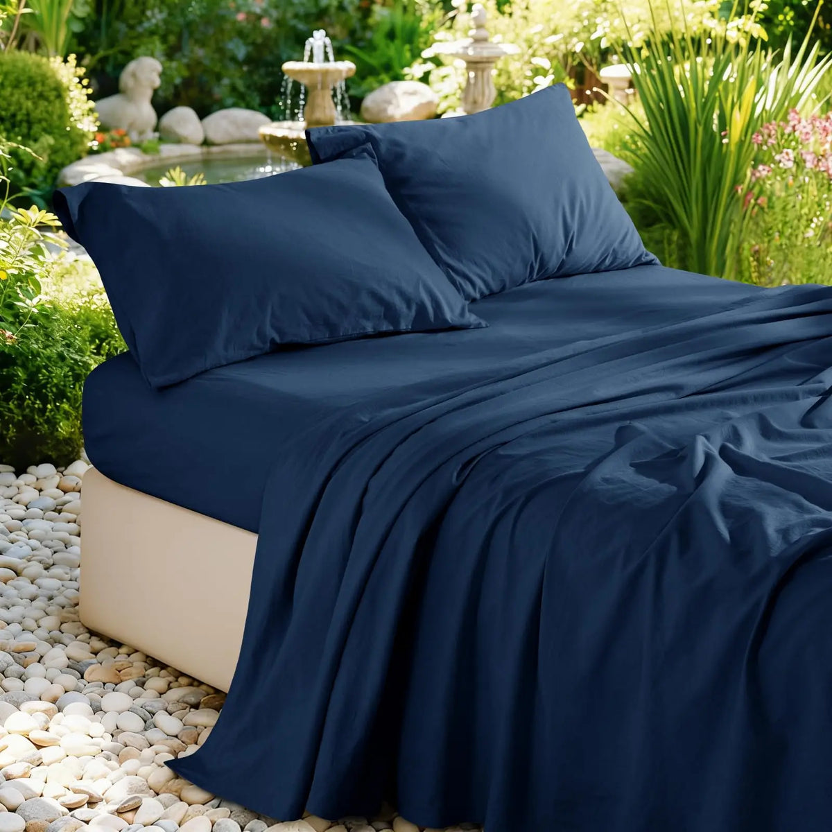 Navy blue pure French linen bed sheet draped on a bed outdoors with lush greenery and stone accents.
