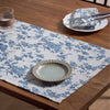 A checkered blue floral table runner on a wooden table with silverware and a plate set.