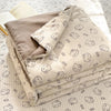 A stack of light beige cartoon quilting comforters with small cat faces on a white background.
