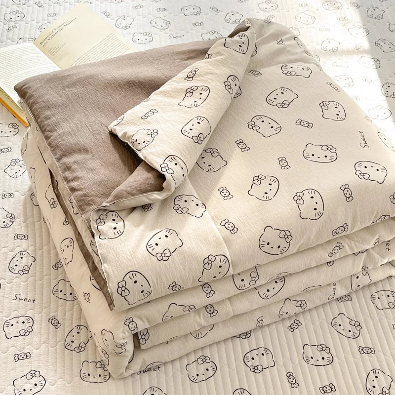 A stack of light beige cartoon quilting comforters with small cat faces on a white background.