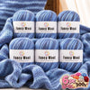 A set of six balls of fancy wool yarn in various shades of blue and gray, packaged for knitting and crochet.