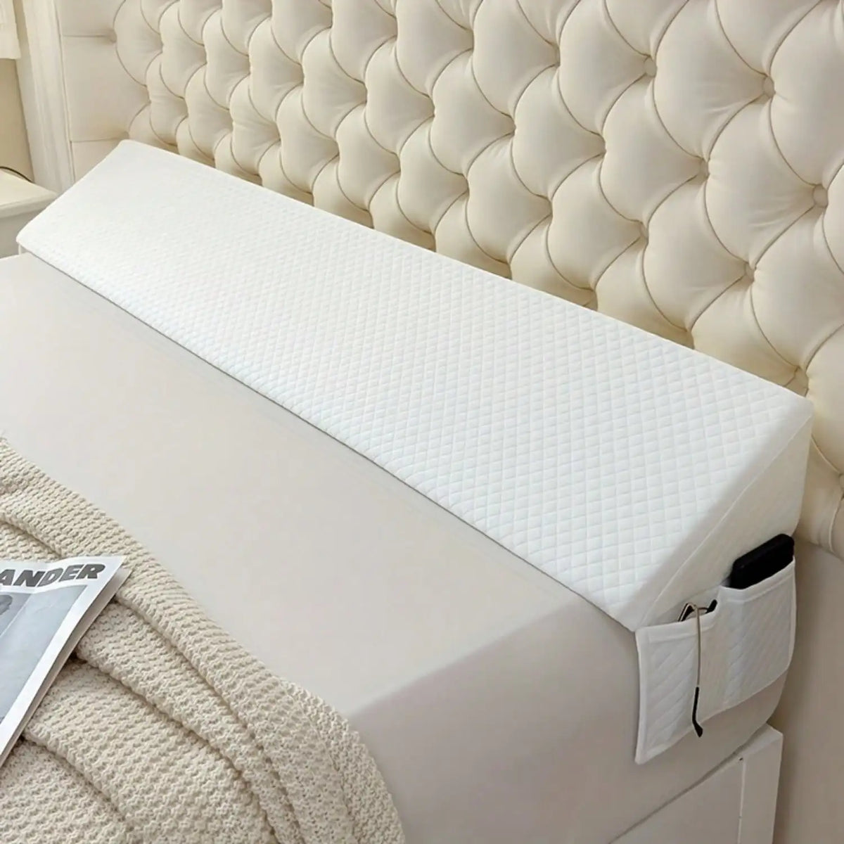 A white adjustable bed wedge pillow with a quilted cover resting on a beige textured blanket.