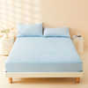 A light blue quilted mattress protector cover lying on a white bed frame with pillows and natural light.