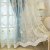Sheer floral curtains in light blue and white lace draped over a window.