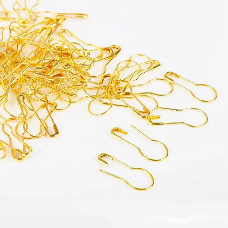 A pile of thin, gold-colored safety bulb pins for knitting and sewing.